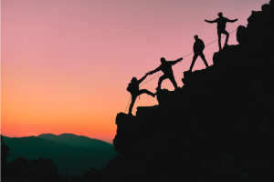 A group of people helping each other up a mountain.