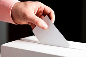 Photograph of someone dropping a ballot in a box.