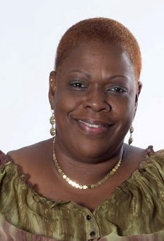 Headshot of an unidentified female of color wearing a gold necklace and green blouse.