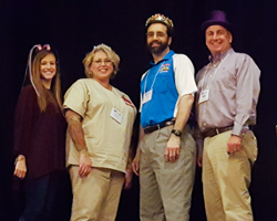 Four people posing for a photo together while wearing various comedic hats. 