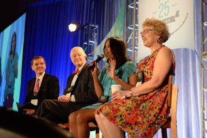 Four panelists sitting on a stage as one of them uses a mic presumably to answer a question.