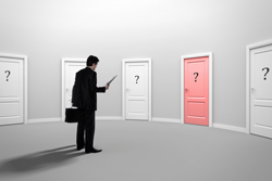 Male in a business suit standing before several plain doors with question marks on them except for one door which is red.