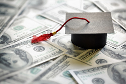 Graduation cap on top of a pile of hundred dollar bills.