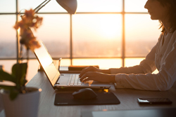 Figure typing on a laptop while sitting at a desk in a window office.