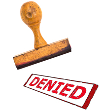 Wooden stamp of the word "denied" in red lettering.