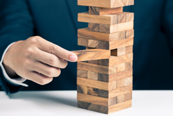 Figure carefully removing a block from a Jenga tower.