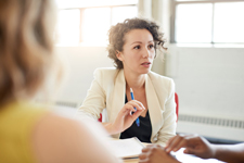 Female wearing a cream colored suit jacket leads a meeting.