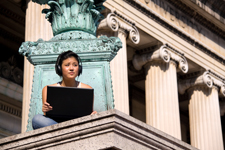 Student wearing headphones and working on their laptop while sitting on top part of a building.