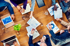 Bird's eye view of a group of people working together around a large wooden table.