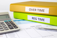 Photo of a time sheet, calculator, and two books. One book is labeled "over time" and the other is labeled "reg time".