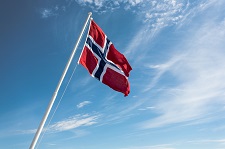 The Norwegian flag rippling in the wind at the top of a flag pole.