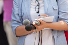 Figure in a baby blue sports jacket holding two microphones and a notepad.