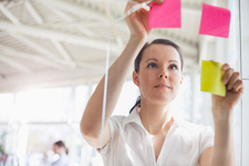 Female arranging pink and lime-green Post-Its on a glass surface.