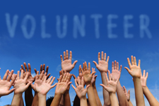 Group of hands raised in the air with the word "volunteer" appearing above the hands.