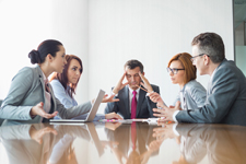 Group of business professionals meeting with the figure in the center appearing to be visibly stressed.