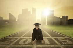 Figure wearing a graduation cap kneeling at a line that says "2015" on an asphalt track.