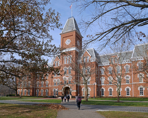 Photo of a large red brick building with a clock tower in its center that appears to be on a college campus.