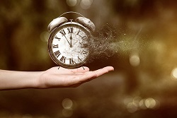 Hand holding an analog alarm clock as it dissolves into dust. 