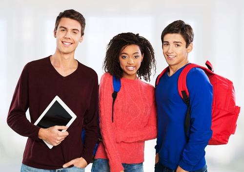 Group of three young students, two of which are wearing backpacks, smile awkwardly at the camera.