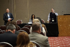 Photo from audience's perspective of three figures standing at the front of an event space.