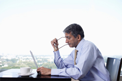 Male dressed in business attire reads something on a laptop while sitting by a window.