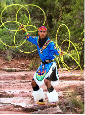 Indigenous person dressed in traditional clothing while dancing with several yellow circles in their hands.